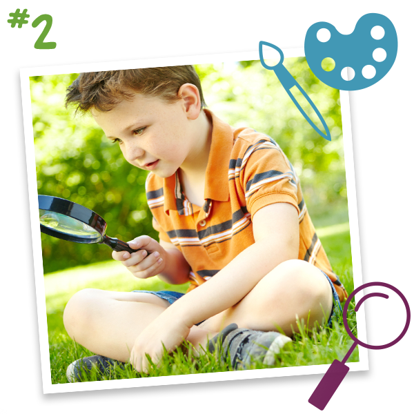 A young boy uses a magnifying glass in the grass.